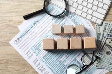 Photo of Taxes. Cubes, money, glasses and documents on light wooden table, flat lay