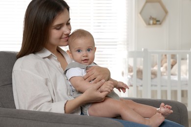 Happy young mother with her baby in armchair at home