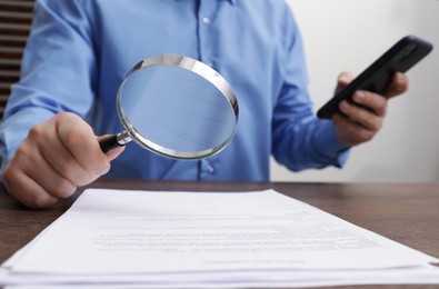 Photo of Man looking at document through magnifier at wooden table, closeup. Searching concept