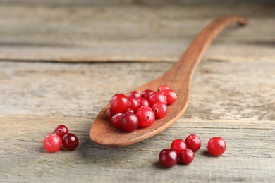 Photo of Cranberries in spoon on wooden table, closeup