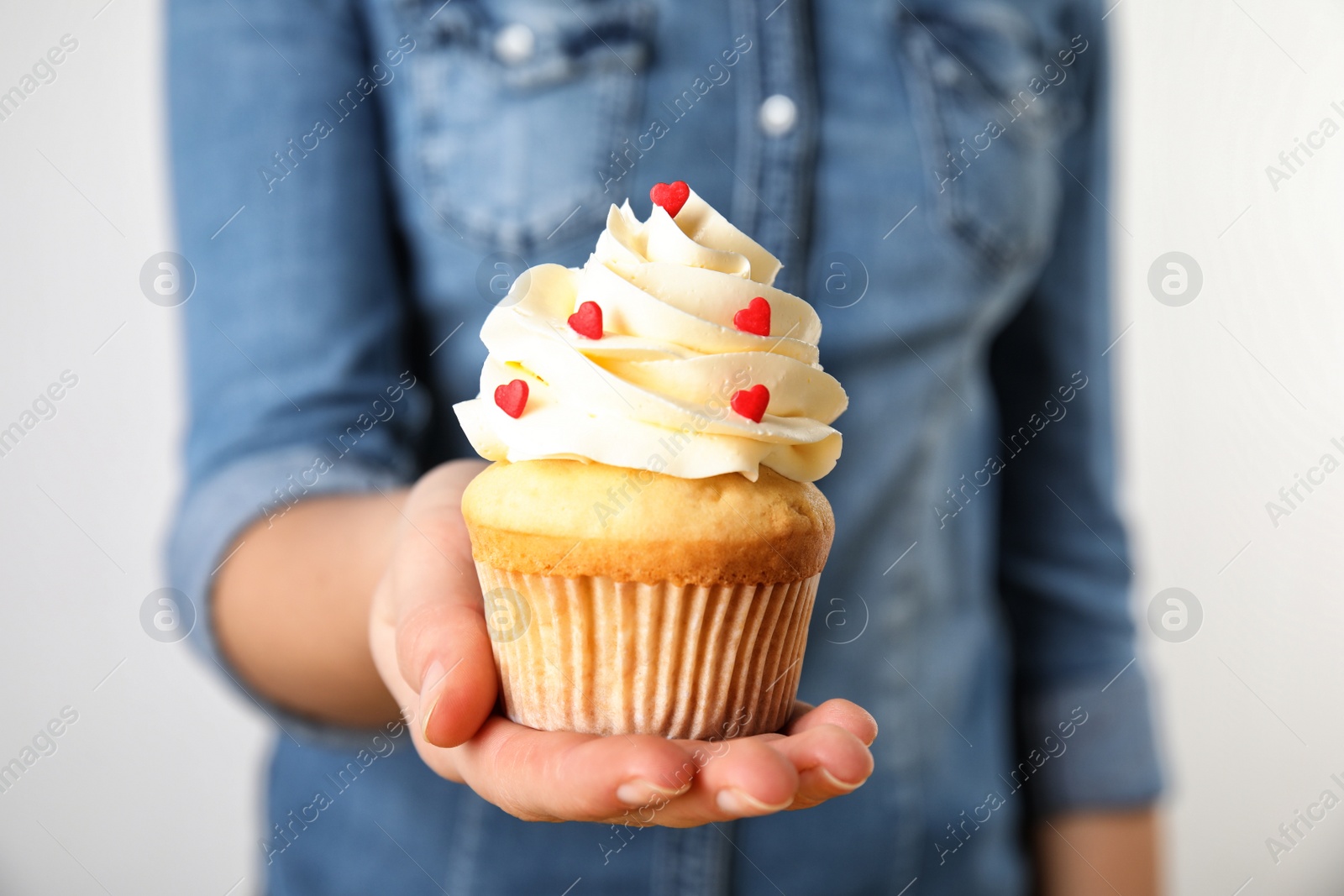 Photo of Woman holding tasty cupcake for Valentine's Day on light background, closeup