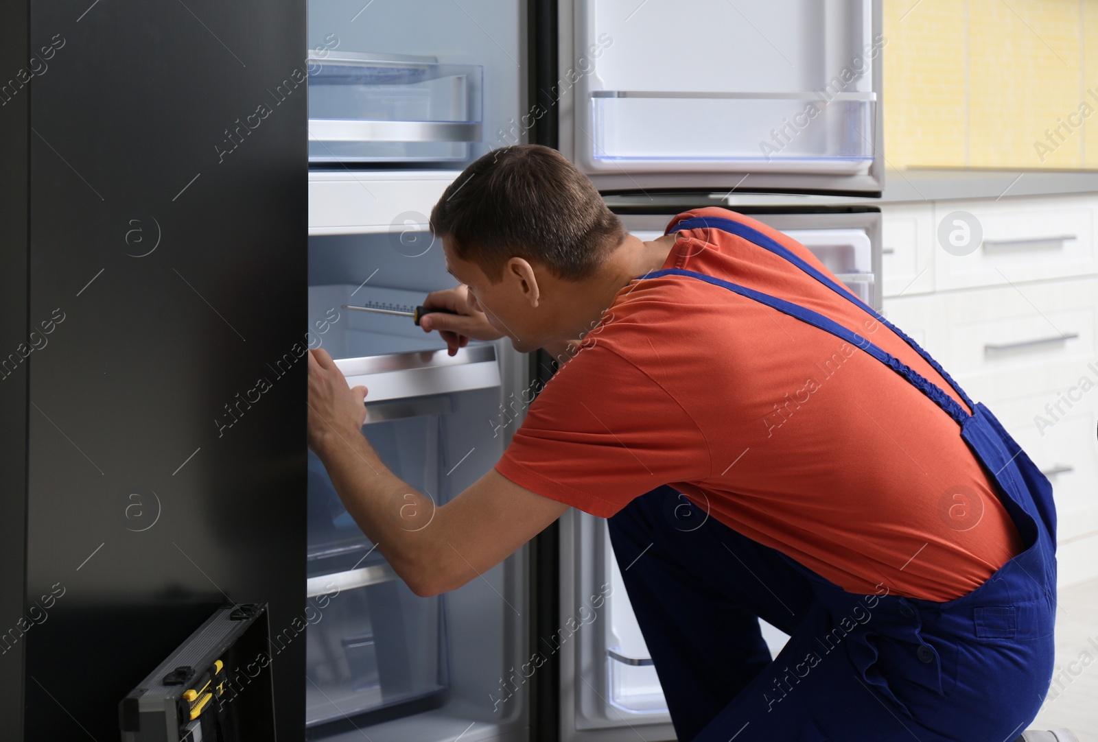 Photo of Male technician with screwdriver repairing refrigerator in kitchen