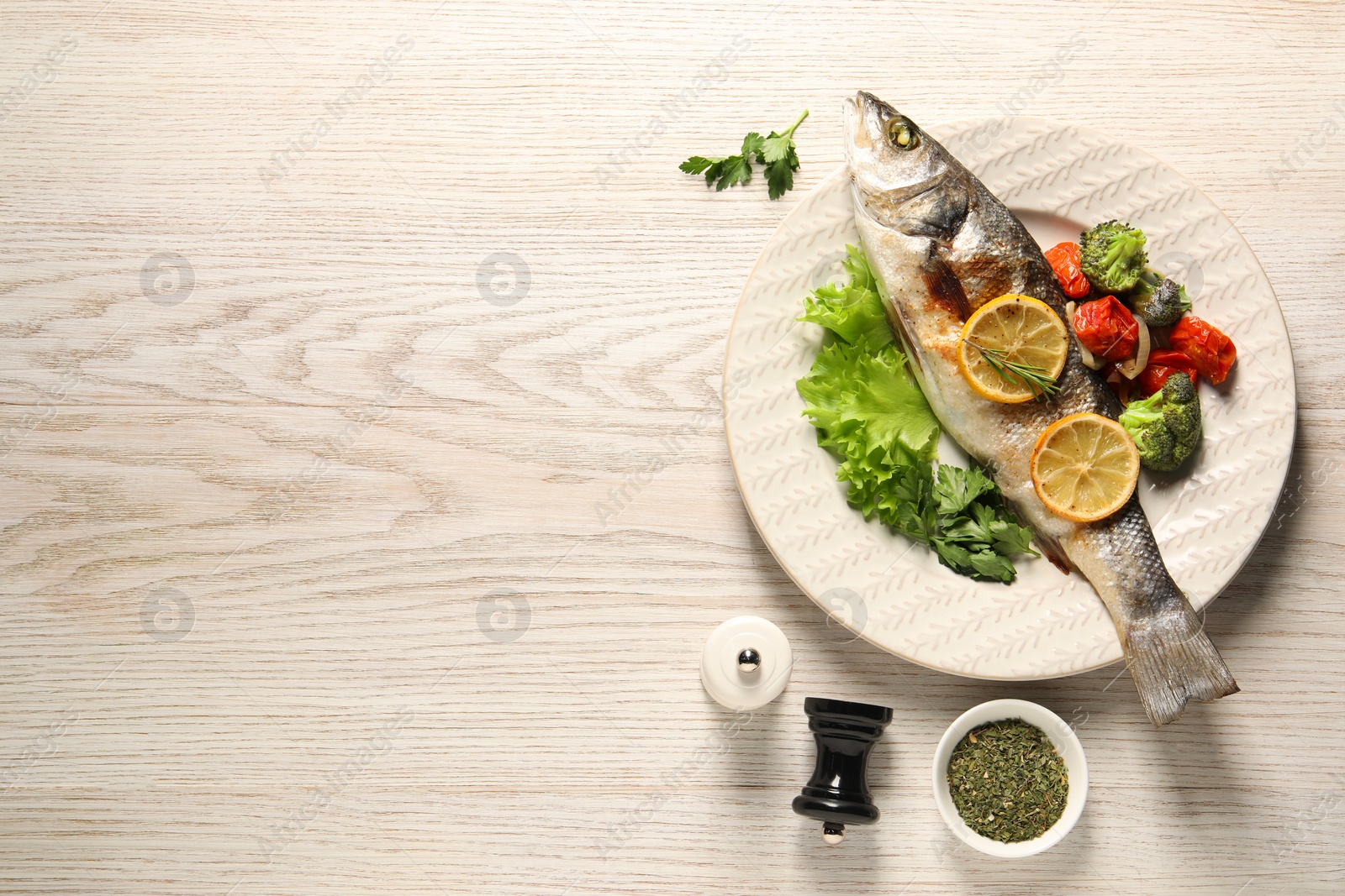 Photo of Delicious baked fish and vegetables served on wooden table, flat lay. Space for text