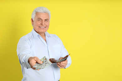 Photo of Happy senior man with cash money and wallet on yellow background. Space for text
