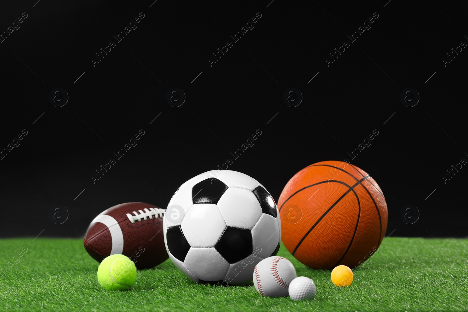 Photo of Many different sports balls on green grass against black background, space for text