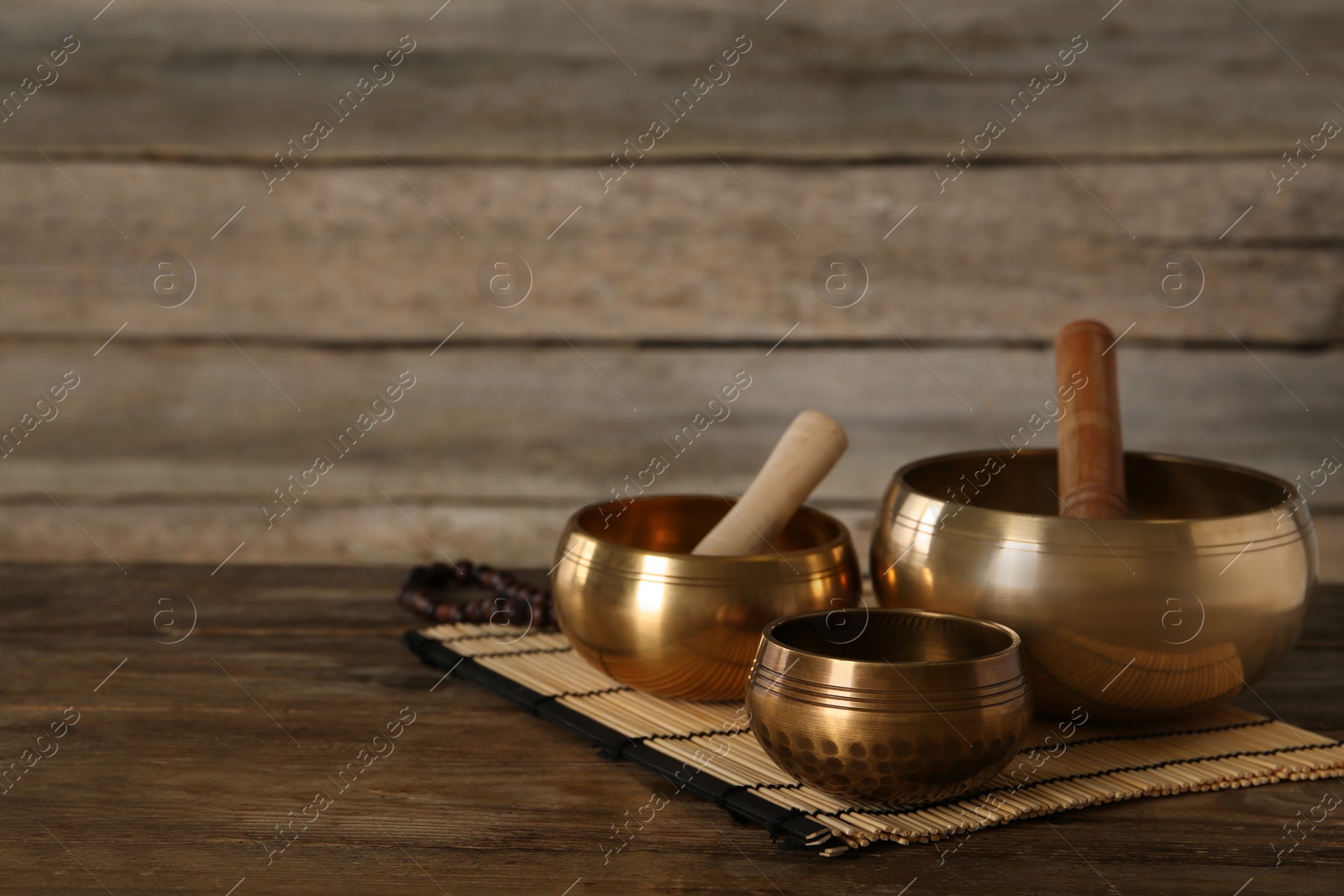 Photo of Golden singing bowls and mallets on wooden table, space for text