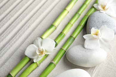 Photo of Bamboo branches with spa stones and orchid flowers on sand