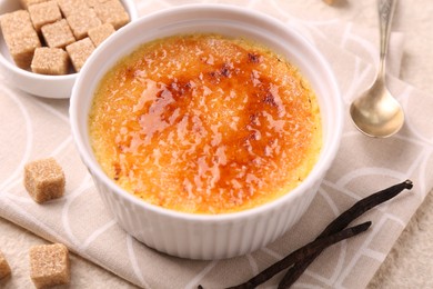 Delicious creme brulee in bowl, vanilla pods and sugar cubes on table, closeup