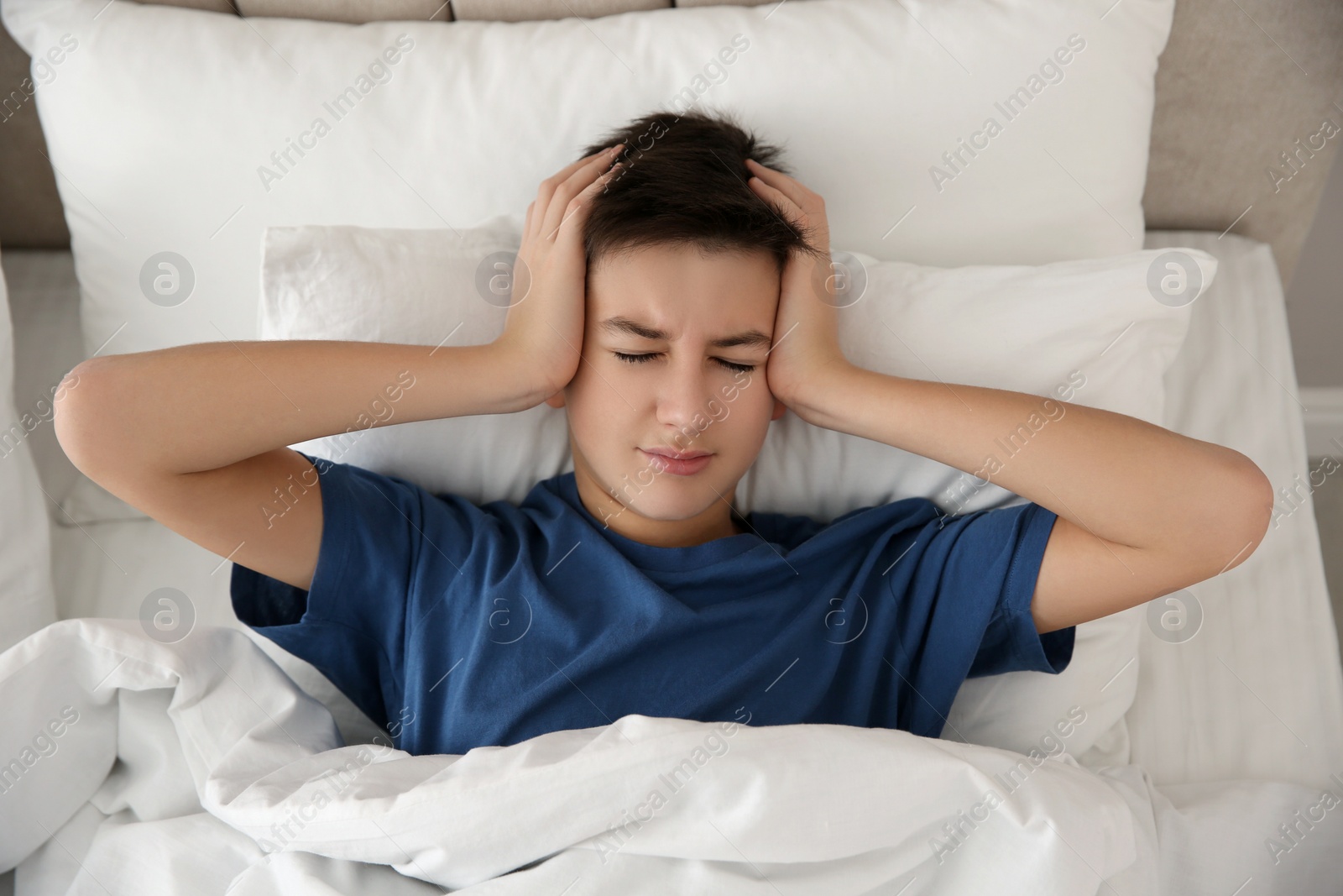 Photo of Cute teenage boy suffering from headache while lying in bed at home, top view