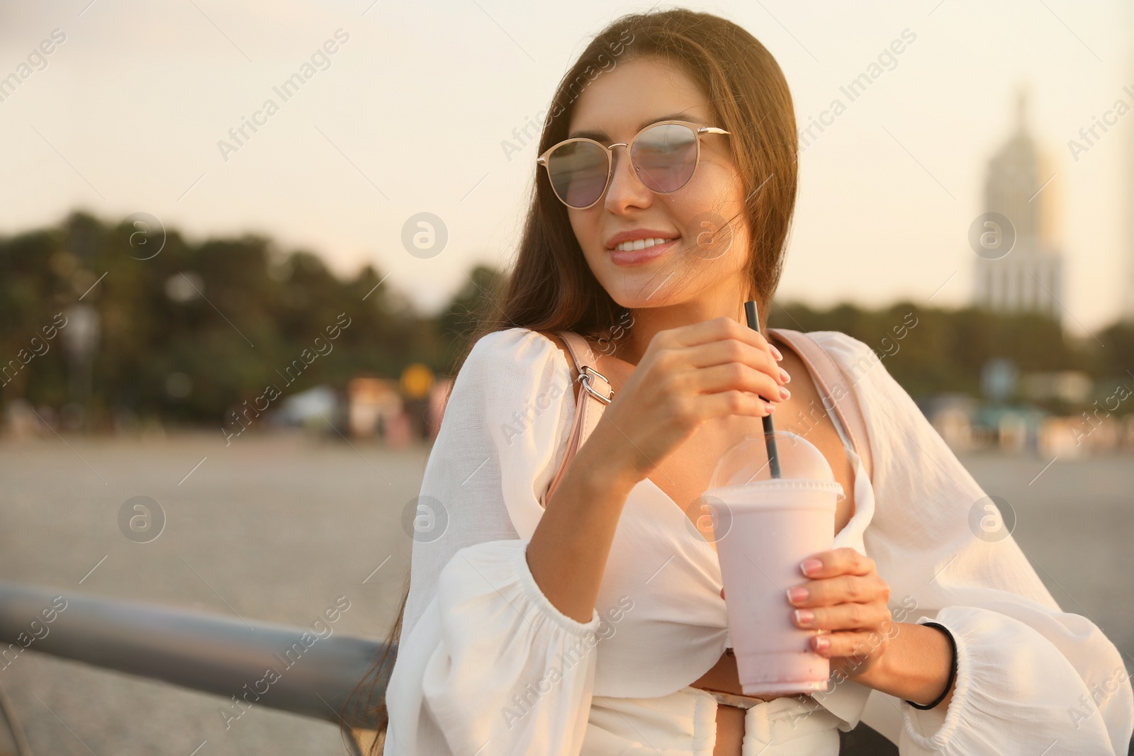 Photo of Beautiful young woman with tasty milk shake outdoors, space for text