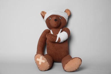 Photo of Toy bear with bandages on light grey background
