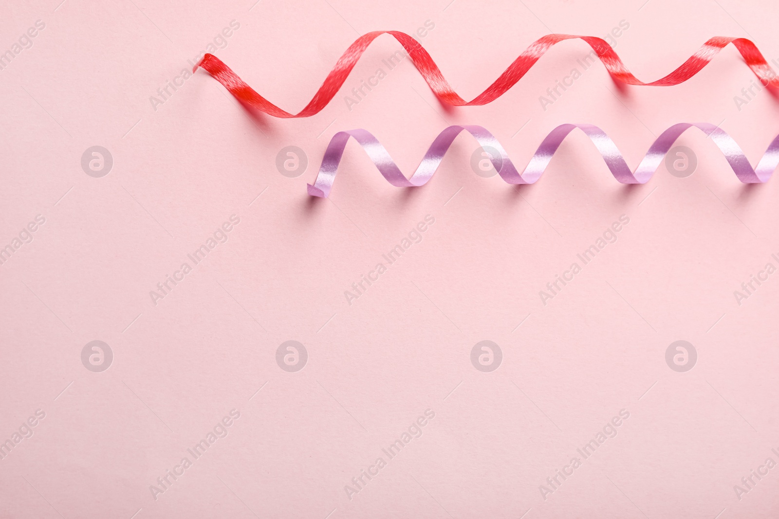 Photo of Colorful serpentine streamers on pink background, flat lay. Space for text
