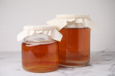 Photo of Tasty kombucha in glass jars on white marble table