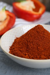 Photo of Bowl with aromatic paprika powder and fresh bell peppers on grey wooden table, closeup