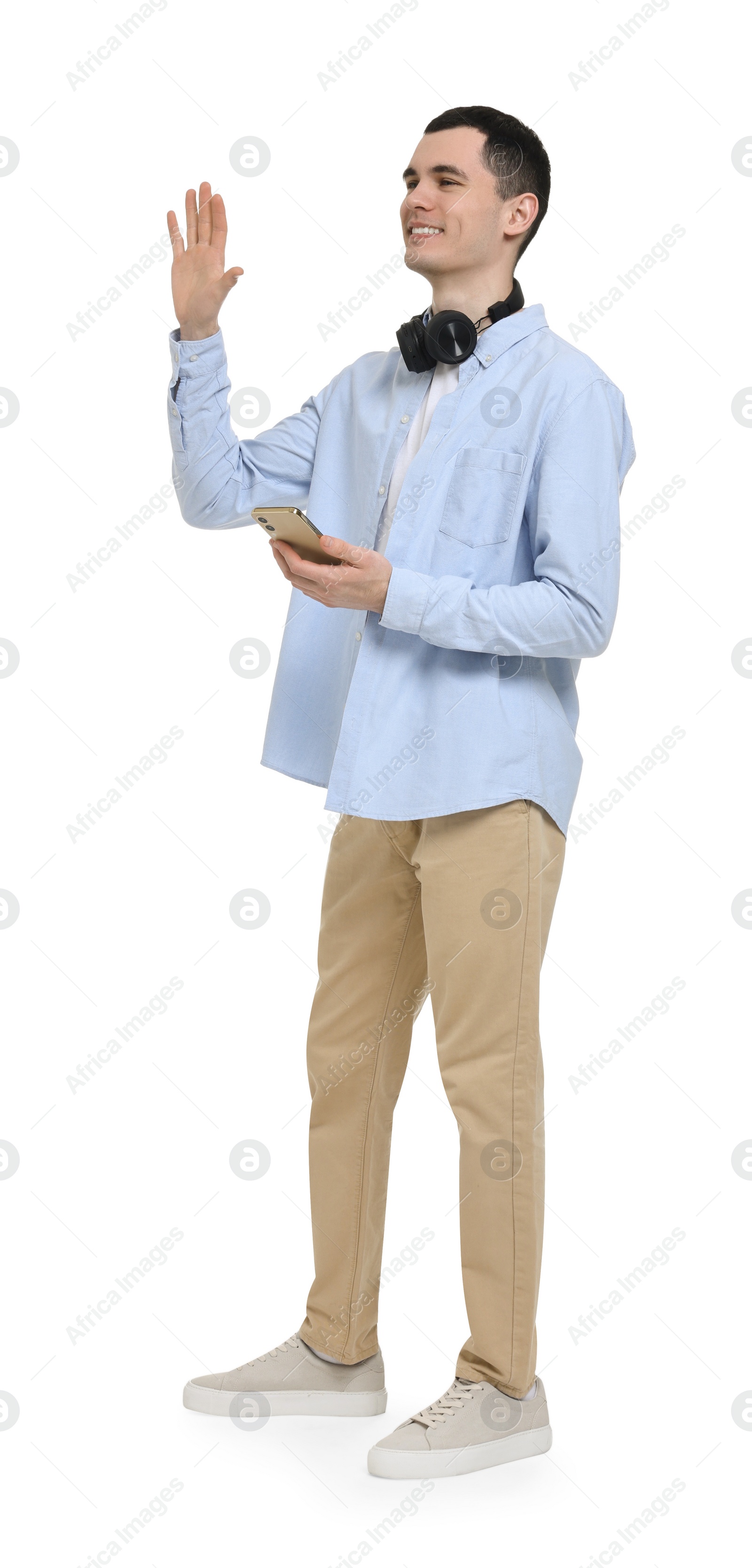 Photo of Young man with headphones and mobile phone waving hand on white background