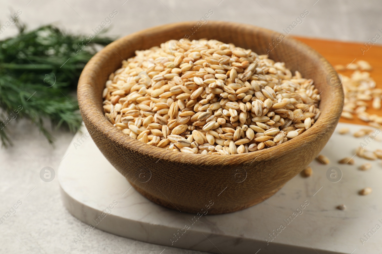 Photo of Dry pearl barley in wooden bowl on table, closeup