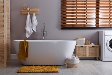 Photo of Soft orange mat on floor near tub in bathroom. Interior design