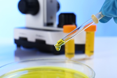 Laboratory assistant dripping urine sample for analysis from pipette into petri dish on table, closeup