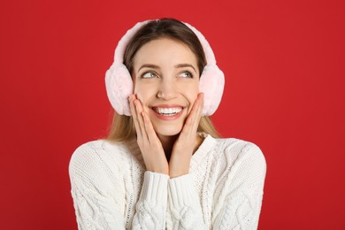 Photo of Happy woman wearing warm earmuffs on red background
