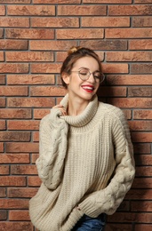 Photo of Beautiful young woman in warm sweater near brick wall