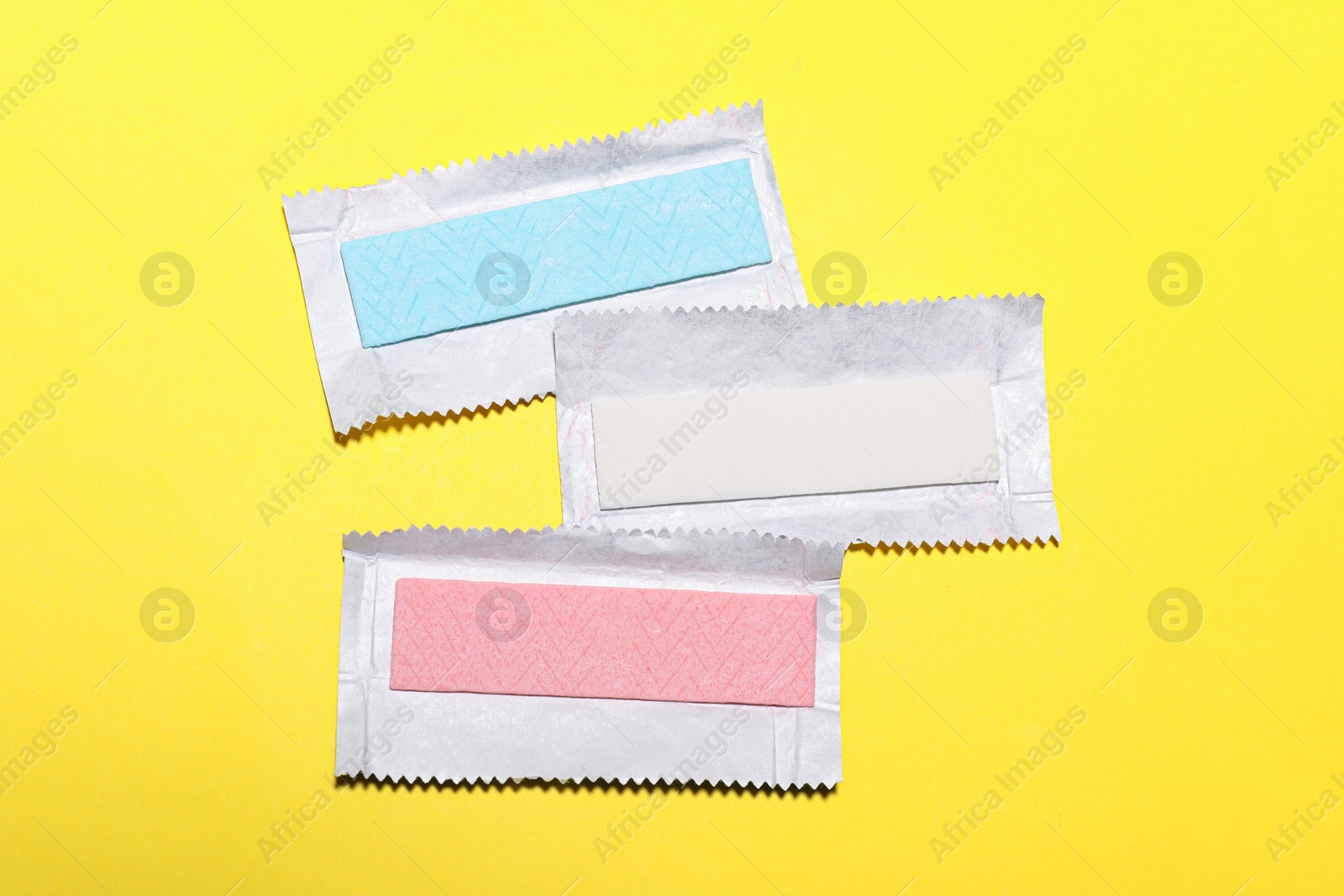 Photo of Unwrapped sticks of tasty chewing gum on yellow background, flat lay