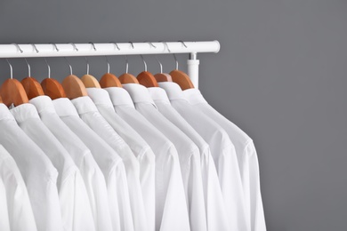 Rack with clean clothes on hangers after dry-cleaning against grey background