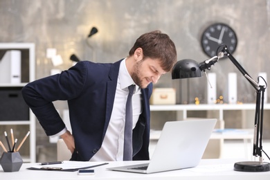 Young man suffering from back pain in office