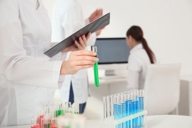 Medical student with test tube and clipboard working in scientific laboratory, closeup