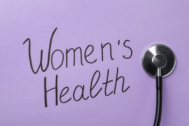 Photo of Stethoscope near text Women's Health on violet background, top view