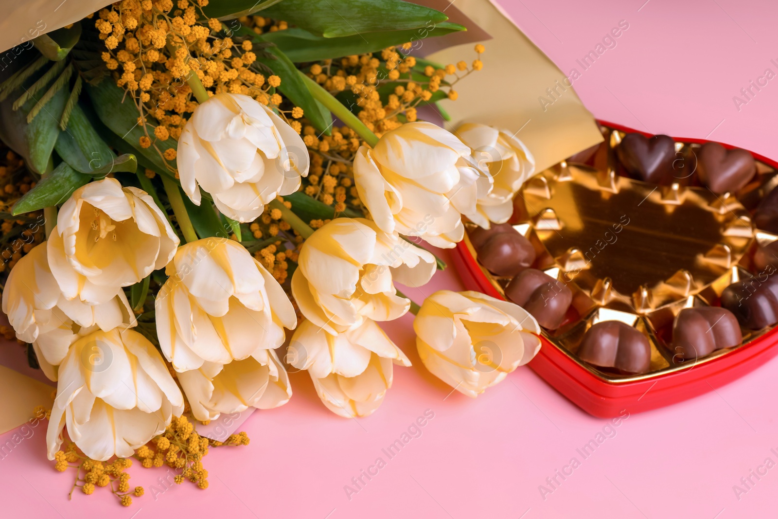 Photo of Bouquet with beautiful tulips, mimosa flowers and box of chocolate candies in shape of heart on pink background