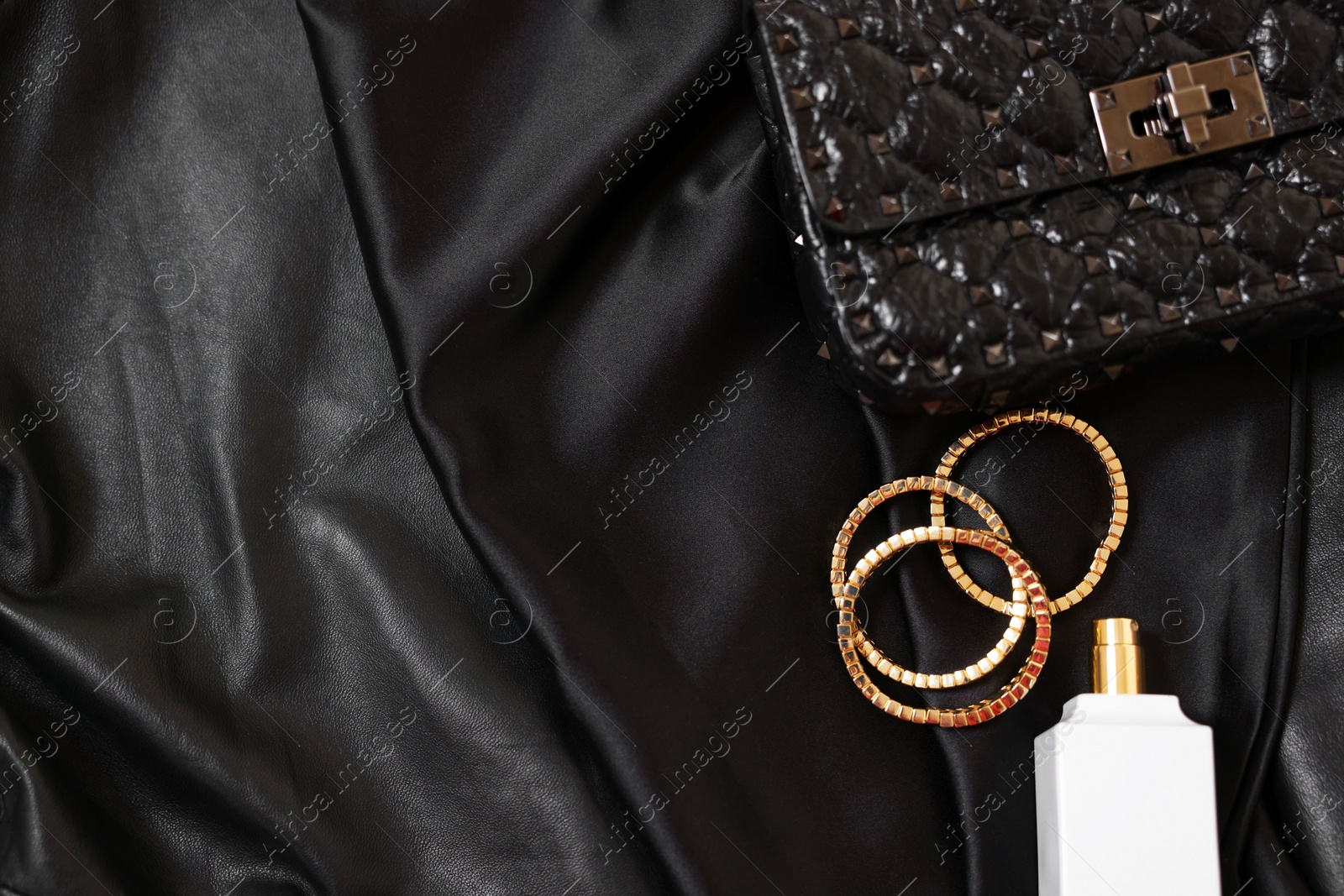 Photo of Leather bag, bottle of perfume and golden bracelets on black fabric, flat lay. Space for text