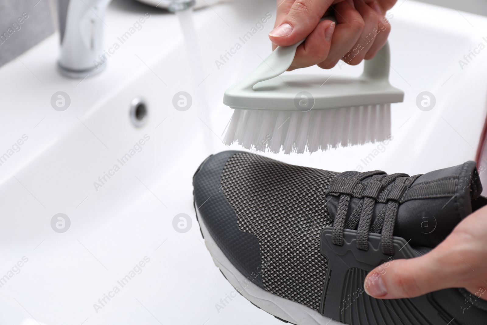 Photo of Woman washing stylish sneakers with brush in sink, closeup