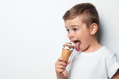 Cute little boy with delicious ice cream against light background