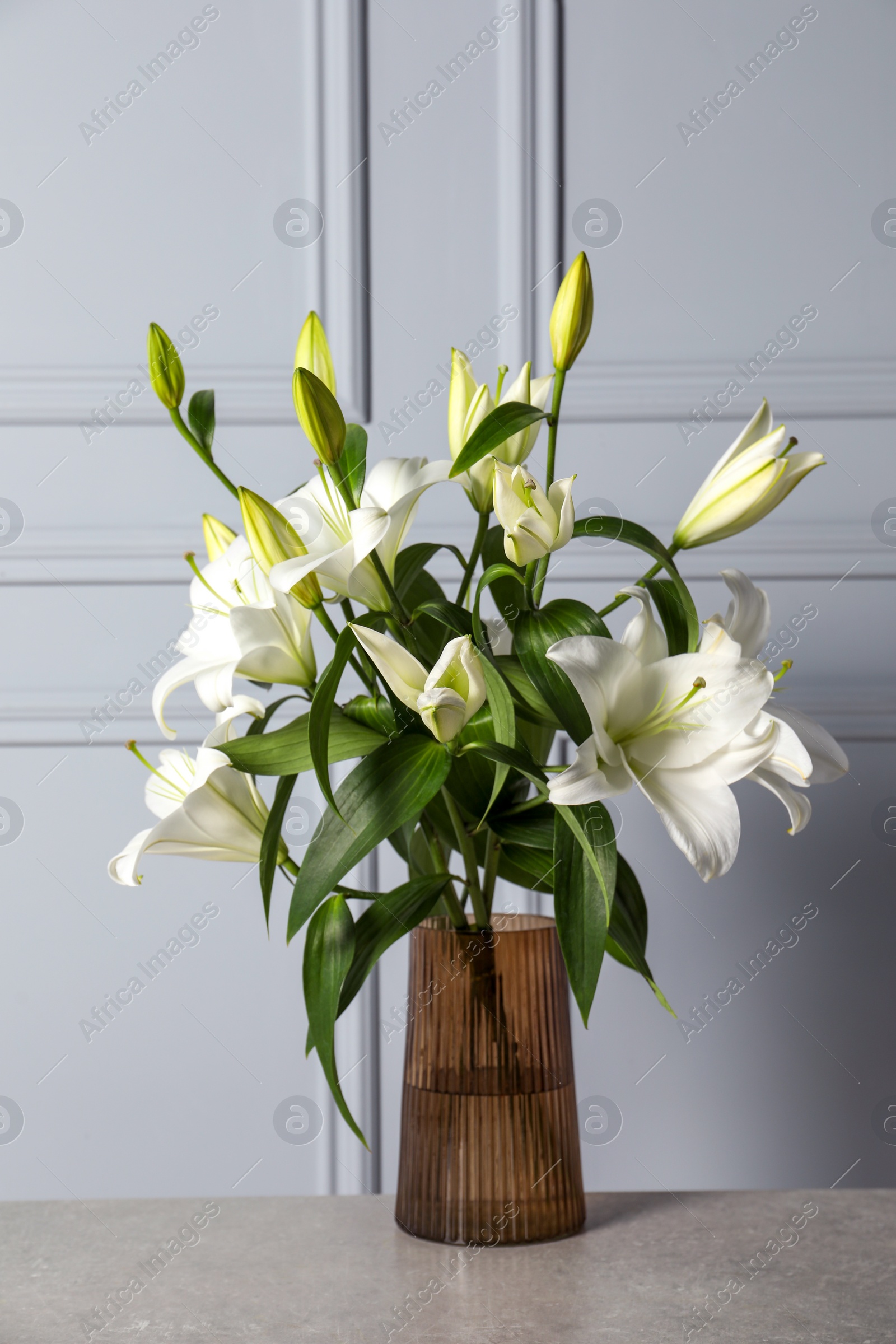 Photo of Beautiful bouquet of lily flowers in glass vase on light grey table