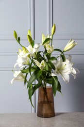 Beautiful bouquet of lily flowers in glass vase on light grey table