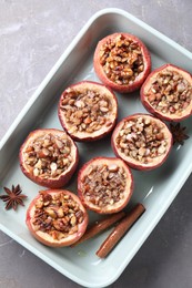 Tasty baked apples with nuts, honey and spices in dish on gray table, top view