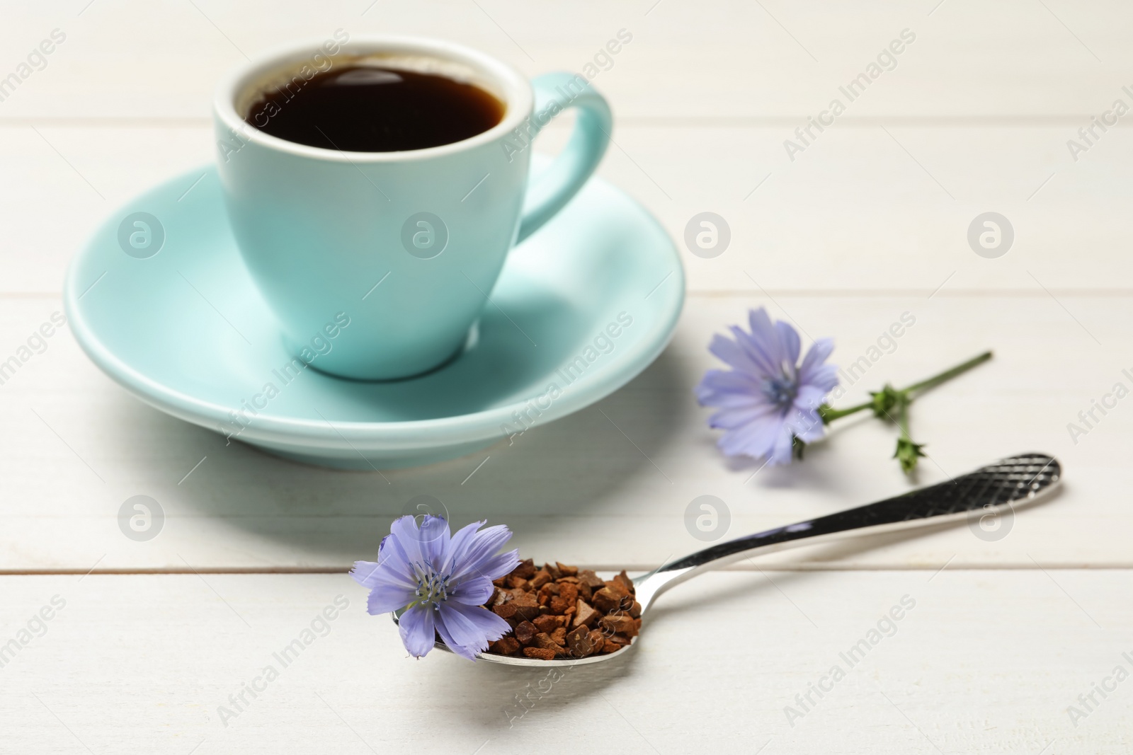 Photo of Spoon of chicory granules with flower on white wooden table