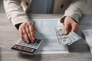 Photo of Payroll. Woman with dollar banknotes and calculator planning budget at wooden table, closeup