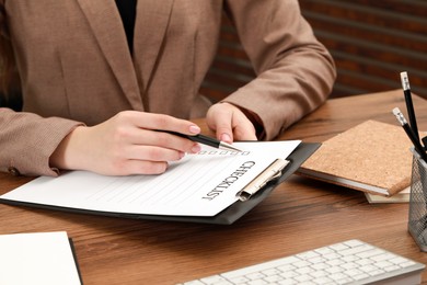 Photo of Woman filling Checklist at wooden table, closeup