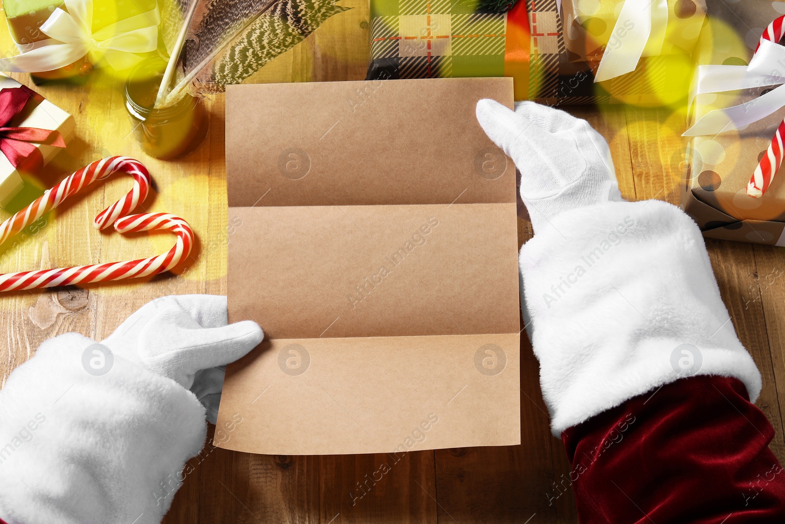 Photo of Santa Claus with letter, gift boxes and Christmas decor at wooden table, above view. Space for text