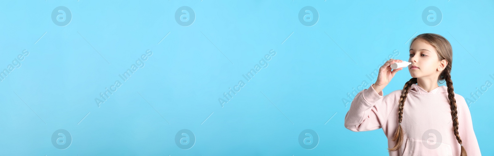 Photo of Sick little girl using nasal spray on light blue background. Space for text