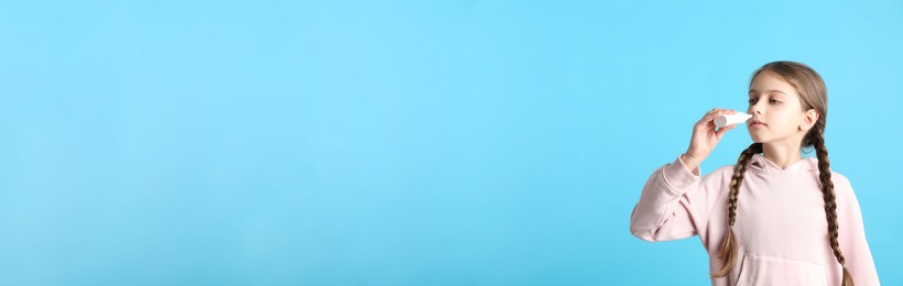 Photo of Sick little girl using nasal spray on light blue background. Space for text