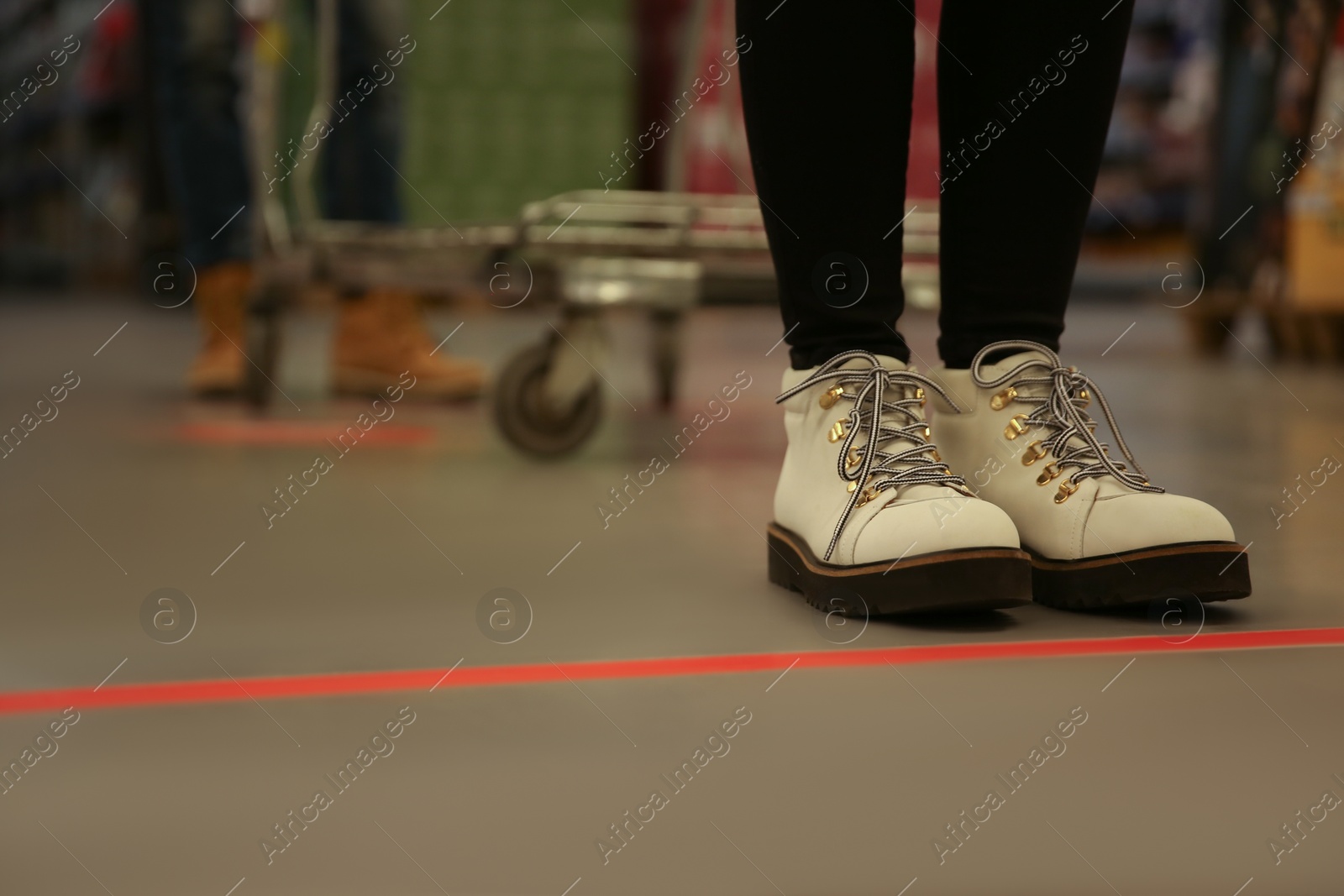 Photo of Woman standing behind taped floor marking in store for social distance, closeup. Preventive measure during coronavirus pandemic