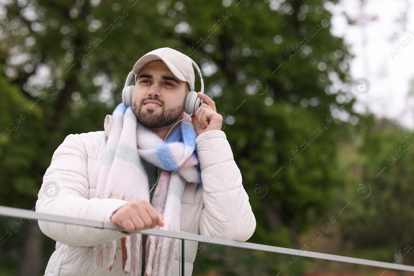 Photo of Smiling man in warm scarf and headphones on blurred background, low angle view. Space for text