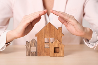 Female agent covering wooden houses at table, closeup. Home insurance