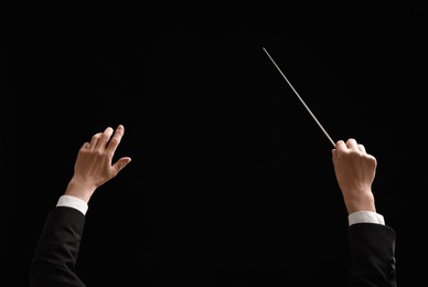 Photo of Back view of professional conductor with baton on black background, closeup