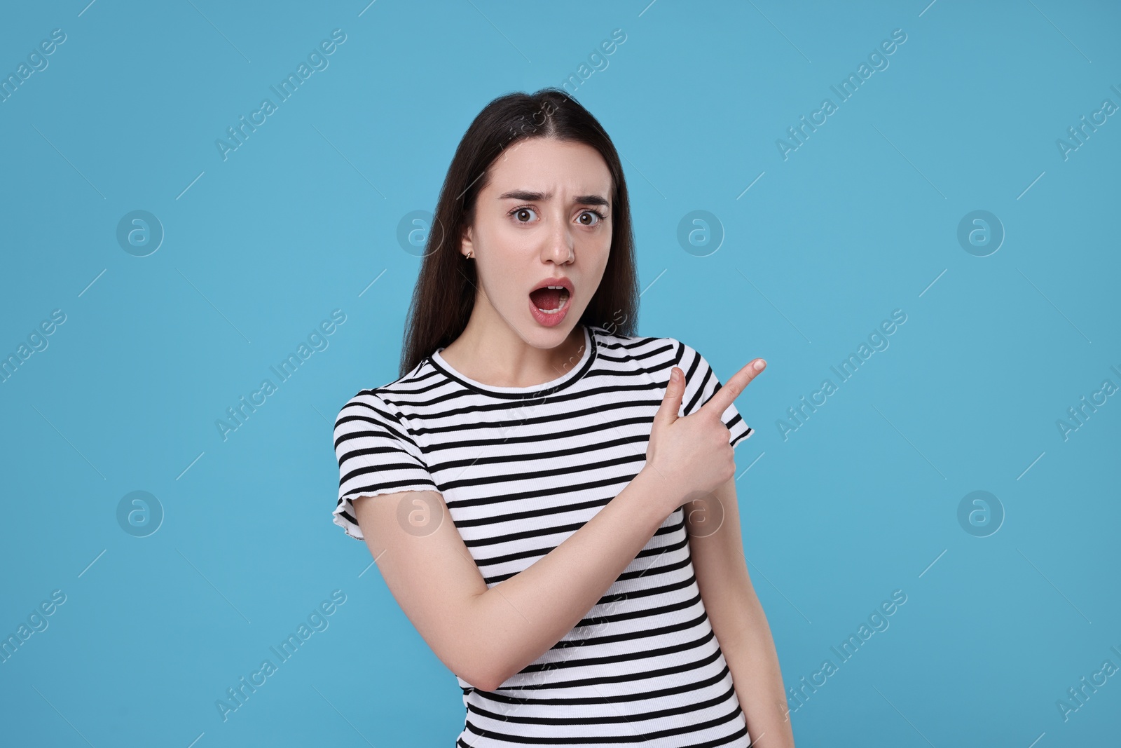 Photo of Portrait of surprised woman pointing at something on light blue background