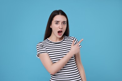 Portrait of surprised woman pointing at something on light blue background