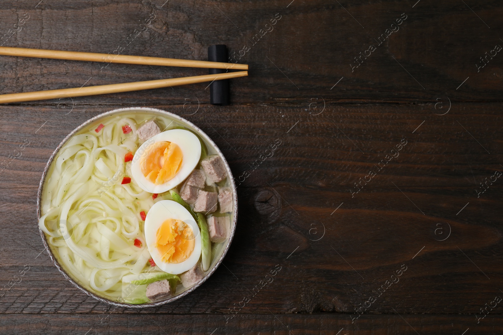 Photo of Bowl of delicious rice noodle soup with meat and egg on wooden table, flat lay. Space for text