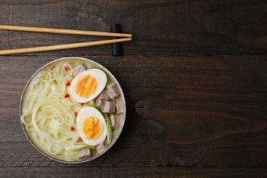 Bowl of delicious rice noodle soup with meat and egg on wooden table, flat lay. Space for text